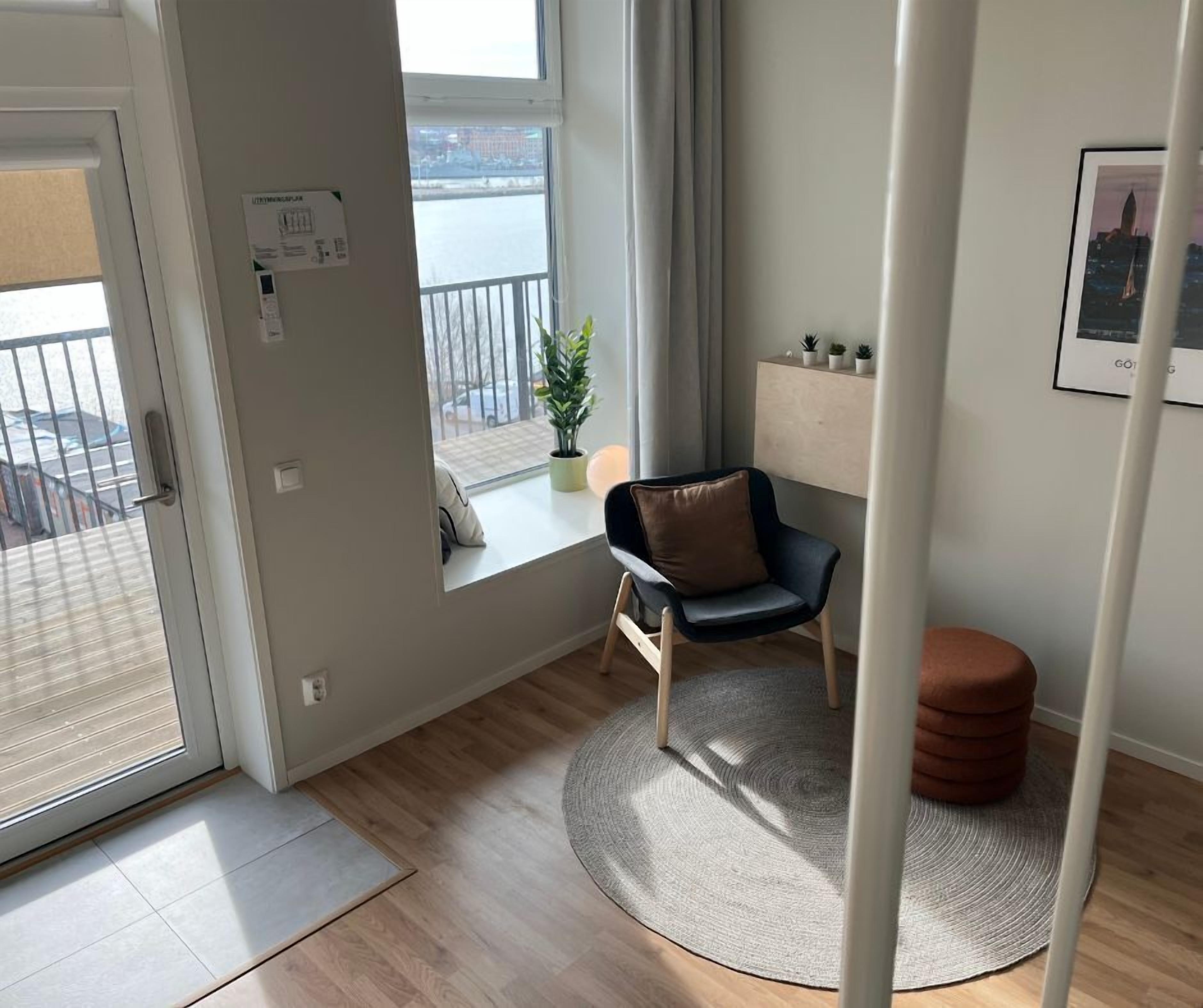 A modern living room with a view of a body of water, a chair, a small table, and a potted plant.