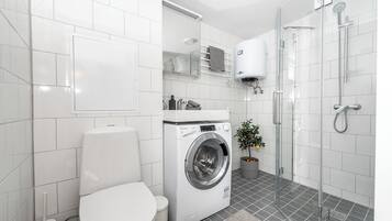 Une salle de bain moderne équipée d’un lave-linge, de toilettes, d’une douche à parois de verre et d’une plante en pot.