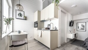 A modern kitchen with white cabinetry, a dining area with a chair, and a small island with a sink. - Waterfront Cabins Studio Apartments (Gothenburg)