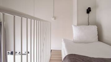 Un dormitorio con una cama, un radiador blanco, una lámpara de pared negra y suelo de madera.