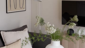 Un salon moderne avec une table ronde blanche, un vase blanc orné de fleurs, un canapé gris et un téléviseur noir fixé au mur.