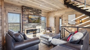 Ein gemütliches Wohnzimmer mit Kamin aus Stein, Ledersofas und einer Holztreppe.