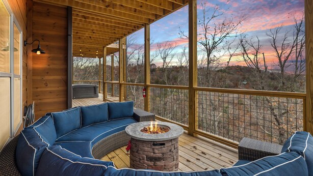 Eine Holzterrasse mit einem Steinkamin, blauen Sitzgelegenheiten und großen Fenstern, die einen Blick auf die Landschaft bieten.