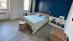 A bedroom with a bed, a small round ottoman, a bookshelf, and a window. - Grand 3 Pieces Lumineux, Lodi (Marseille)