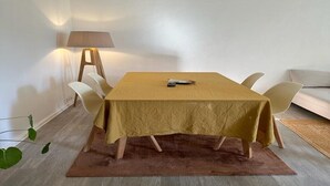 A dining area with a table covered by a yellow tablecloth, surrounded by white chairs, and a lamp on the side. - Grand 3 Pieces Lumineux, Lodi (Marseille)