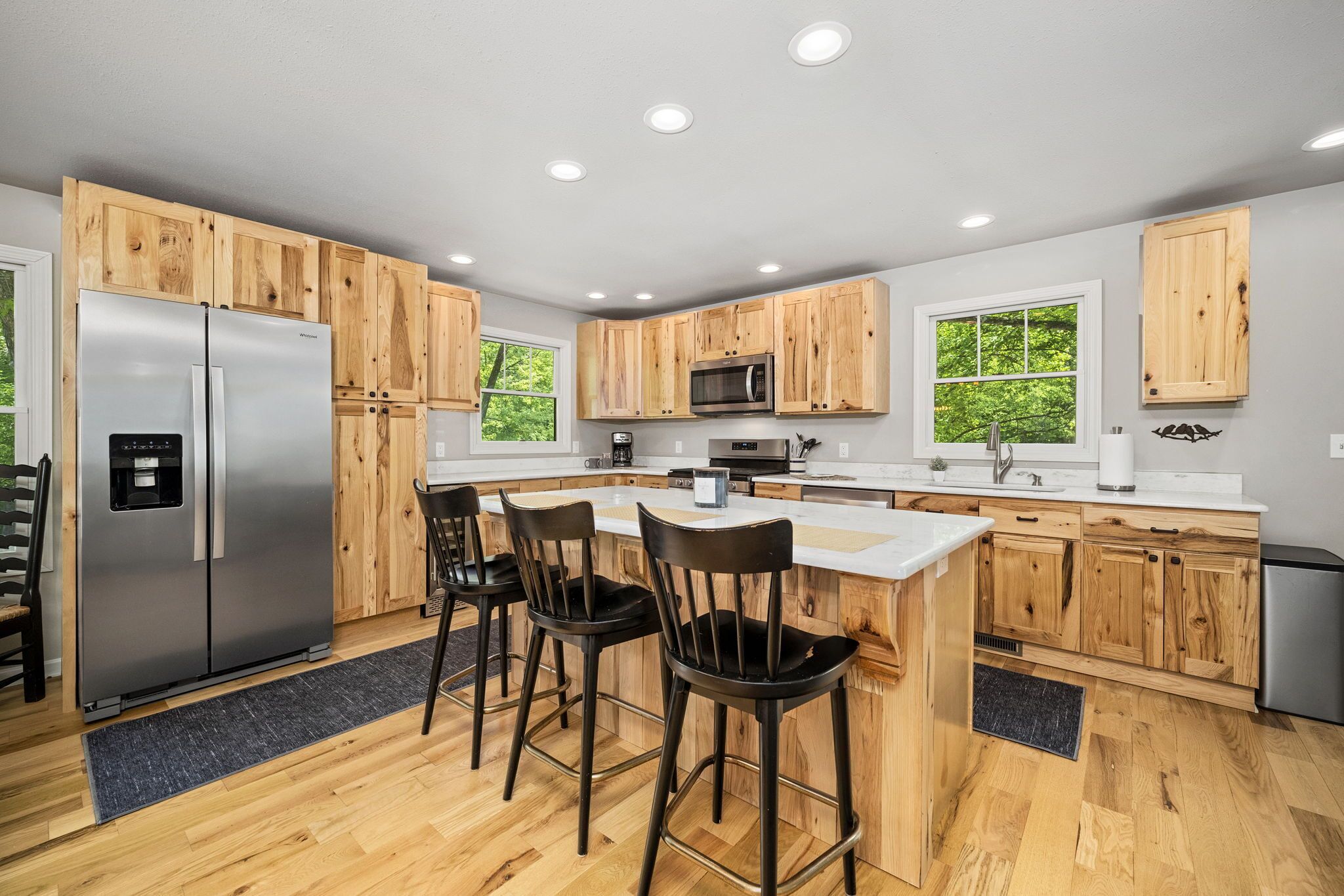 A modern kitchen with wooden cabinets, stainless steel appliances, a bar area, and large windows.
