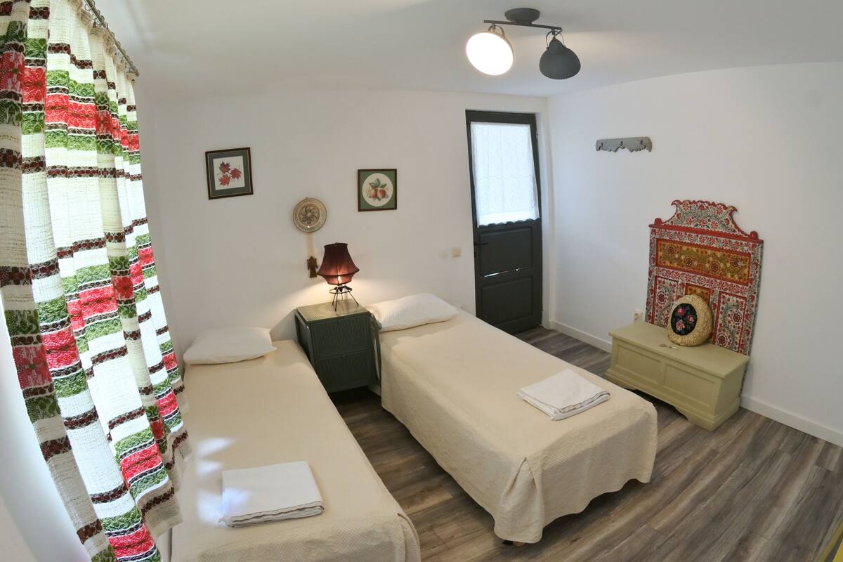 A room with two single beds, a small bedside table with a lamp, a door, and a wall-mounted decorative item.