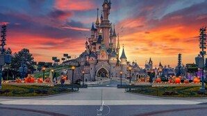 Une structure ressemblant à un château, dotée de nombreuses tours et de flèches, entourée d’une zone pavée agrémentée d’éléments décoratifs.