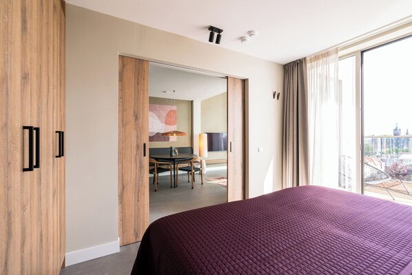 A modern hotel room with a large bed, a dining area, and a view of the city. - BizStay Walden (The Hague)