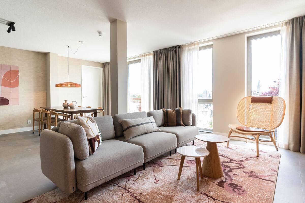 A modern living room with a sectional sofa, a dining table, and a wicker chair.