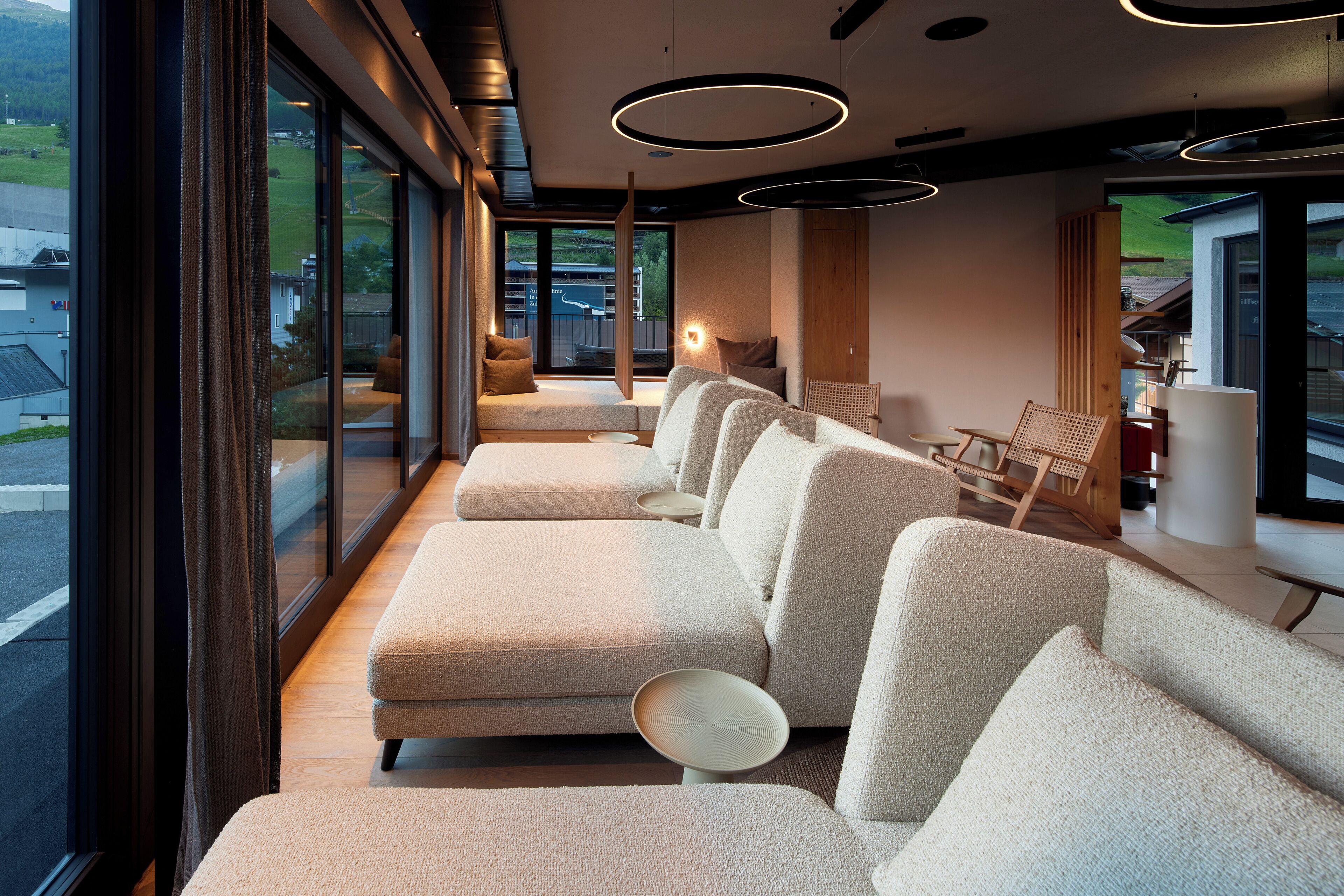 A modern interior with a row of sofas facing a large window, a wooden bench, and a table with chairs.