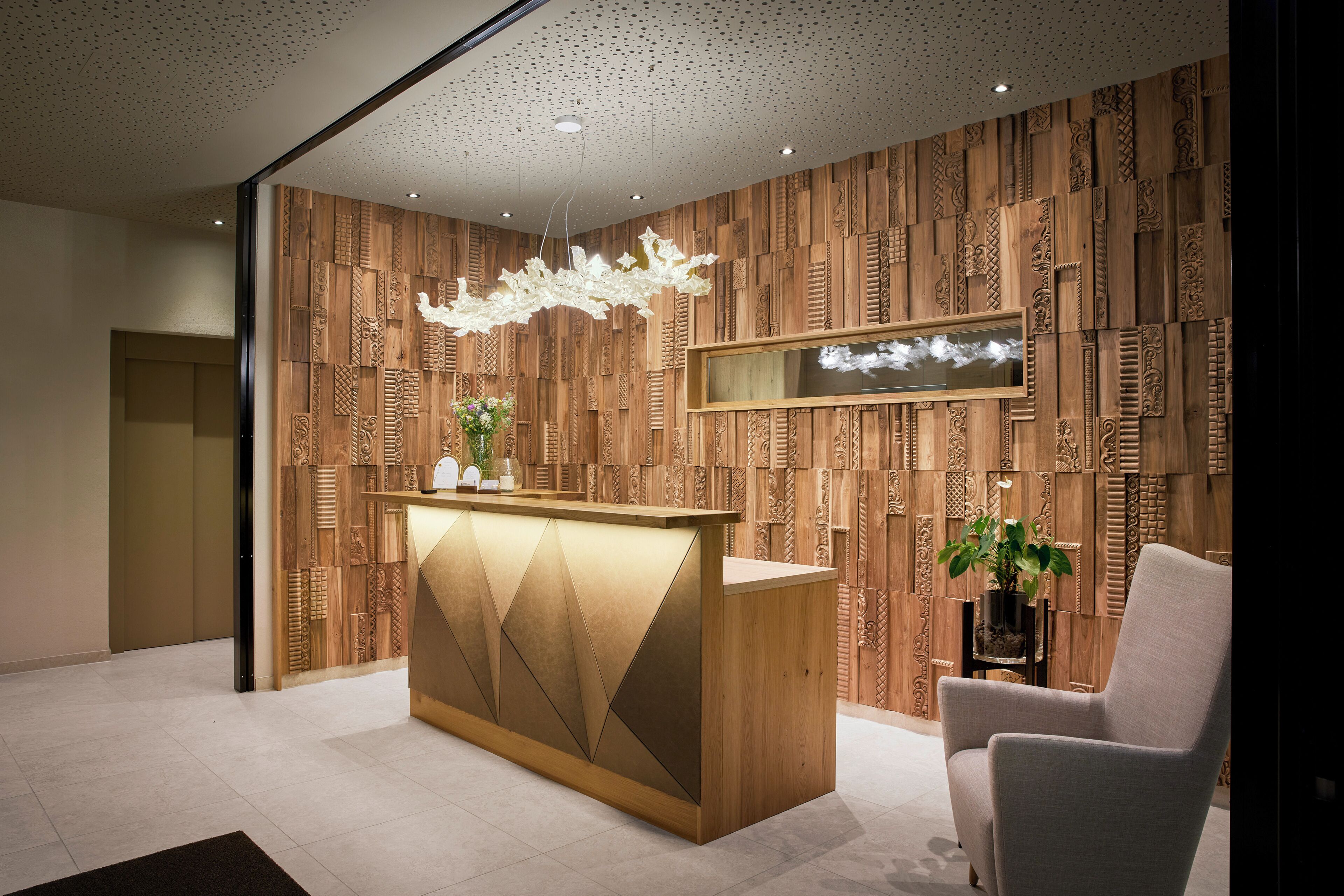 Una recepción con un diseño geométrico, una lámpara de araña moderna y un panel de pared de madera con intrincados relieves.