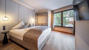 Un dormitorio moderno con una cama grande, una mesita de noche, una lámpara colgante y una ventana con vistas a árboles.