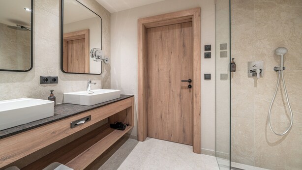 A modern bathroom with a wooden door, a glass shower enclosure, and a large mirror. - Edelweiss echt.charmant. (Soelden)