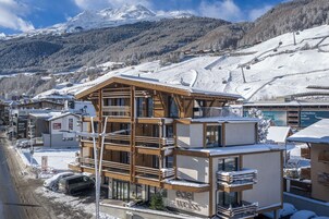 Un hotel de varios pisos con una pista de esquí al fondo, balcones de madera y un cartel que dice Edel Weiss.