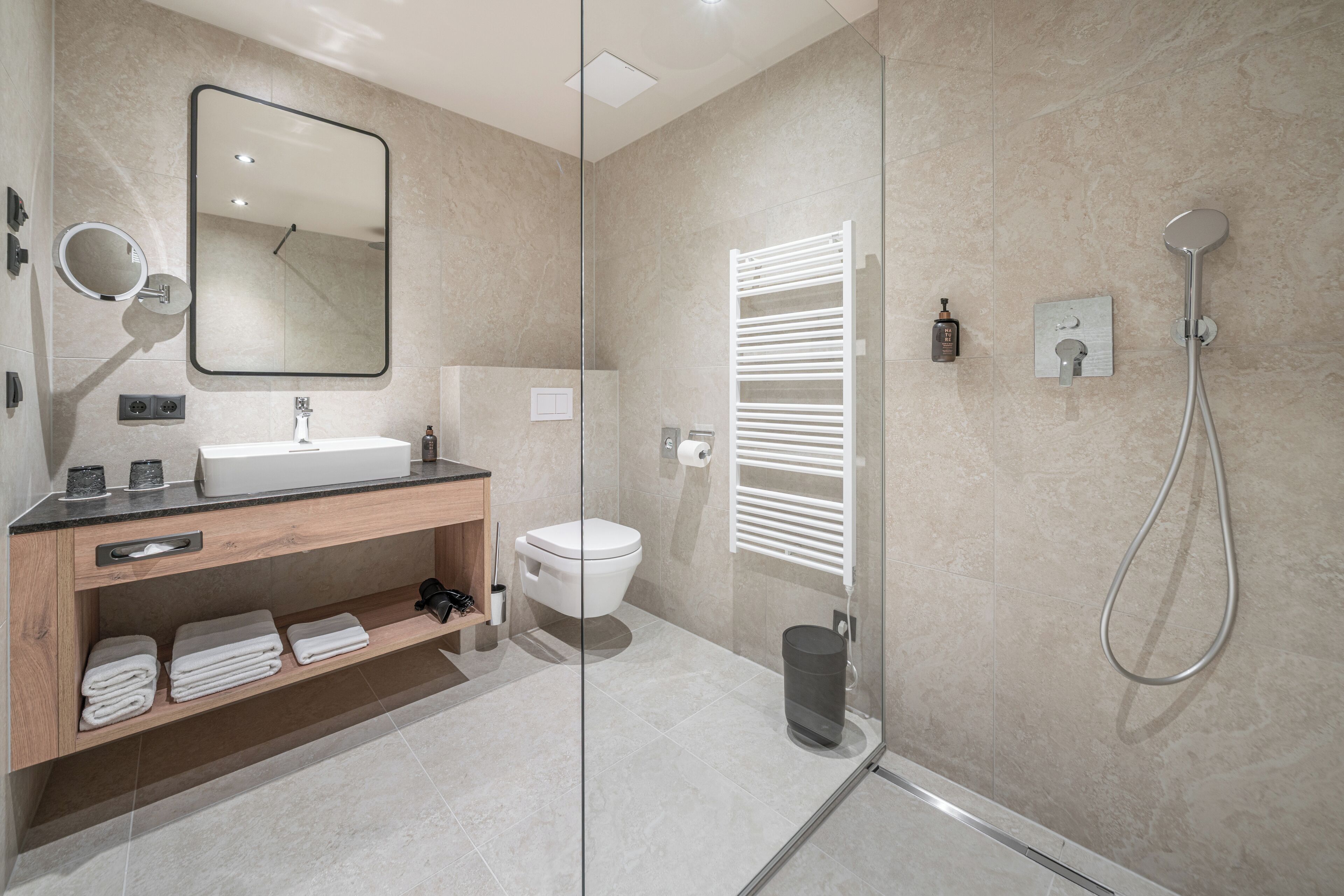 A modern bathroom with a glass shower enclosure, a white toilet, a wooden vanity with a mirror, and a towel rack.