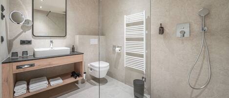 A modern bathroom with a glass shower enclosure, a white toilet, a wooden vanity with a mirror, and a towel rack.