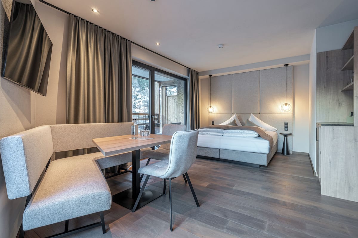 A modern hotel room with a sofa, a dining table, a bed, and a small bedside table.