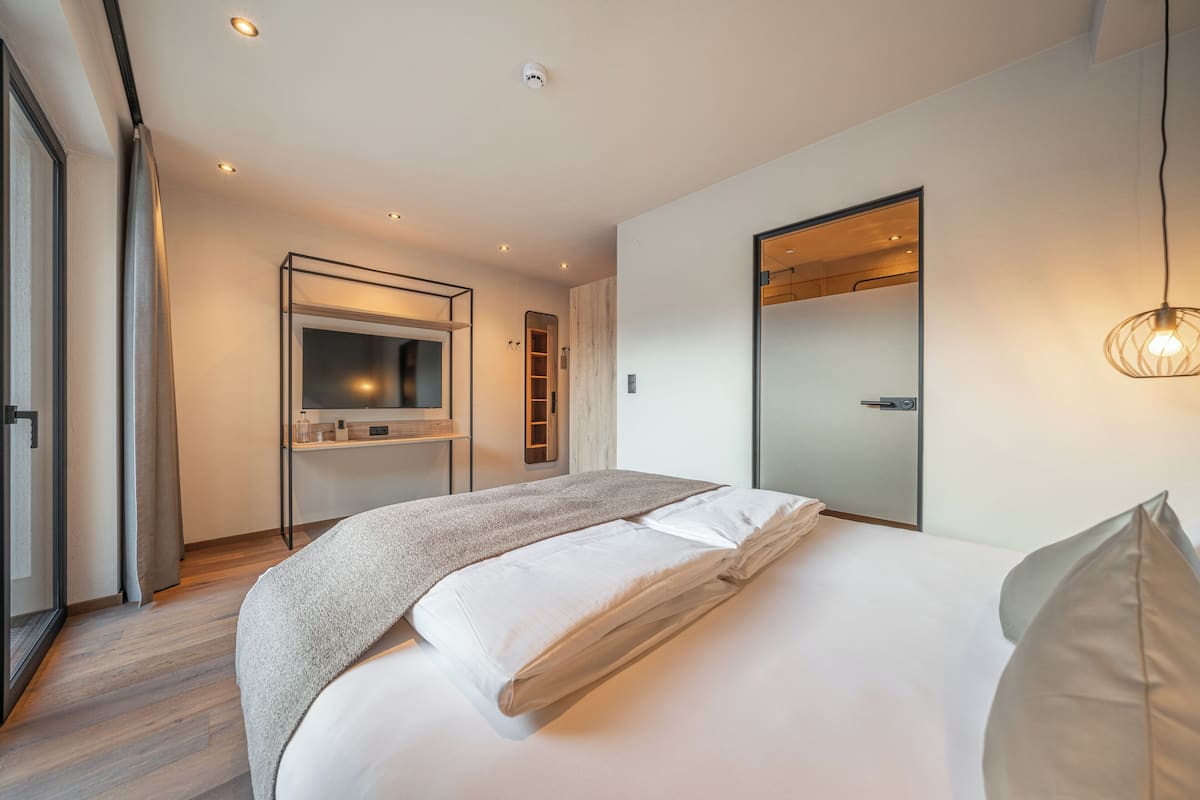 A modern hotel room with a large bed, a built-in TV, a mirror, and a sliding door.