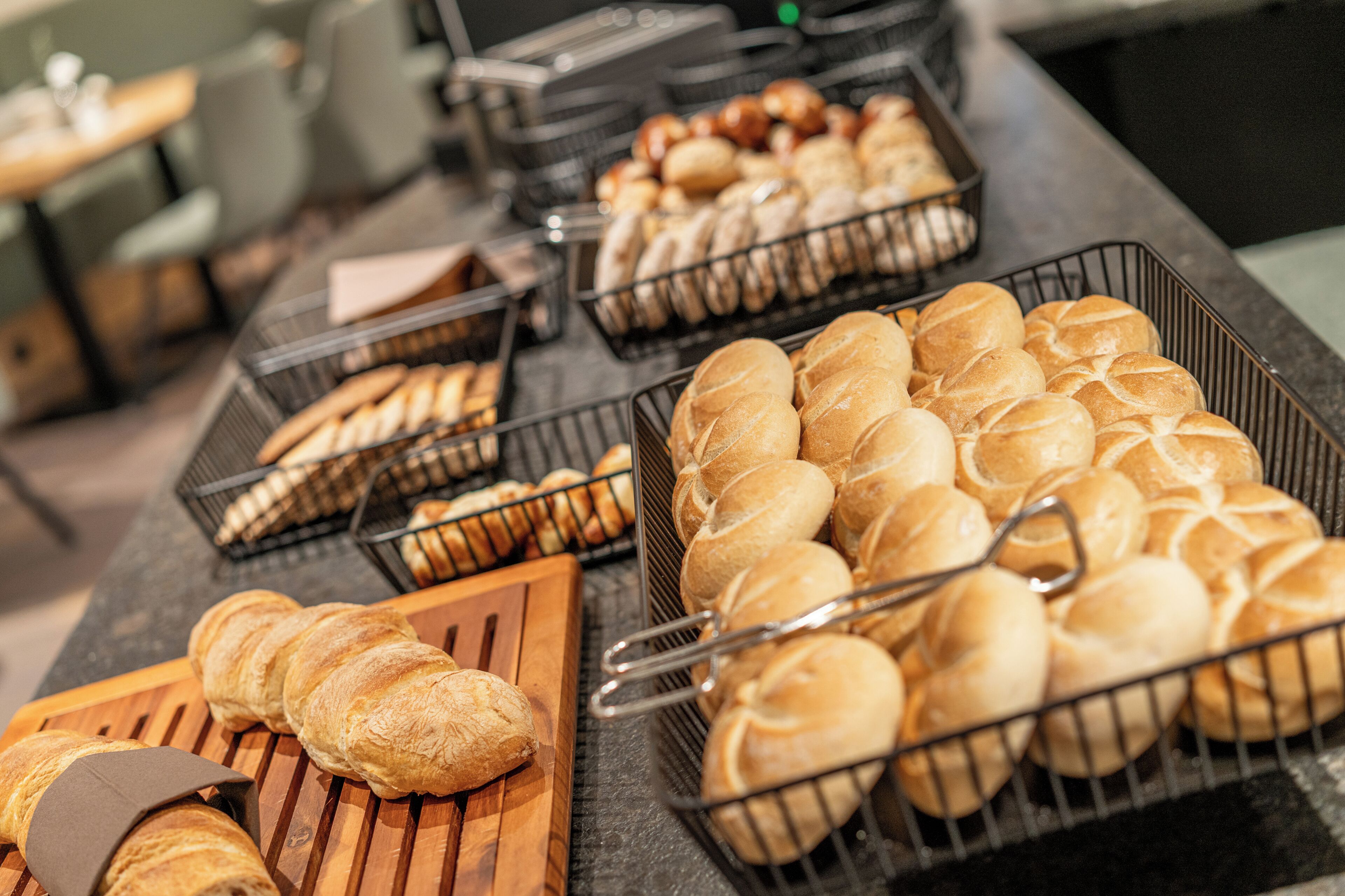 Ein Buffet mit verschiedenen Backwaren, darunter Brötchen und Croissants, in Drahtkörben angerichtet.