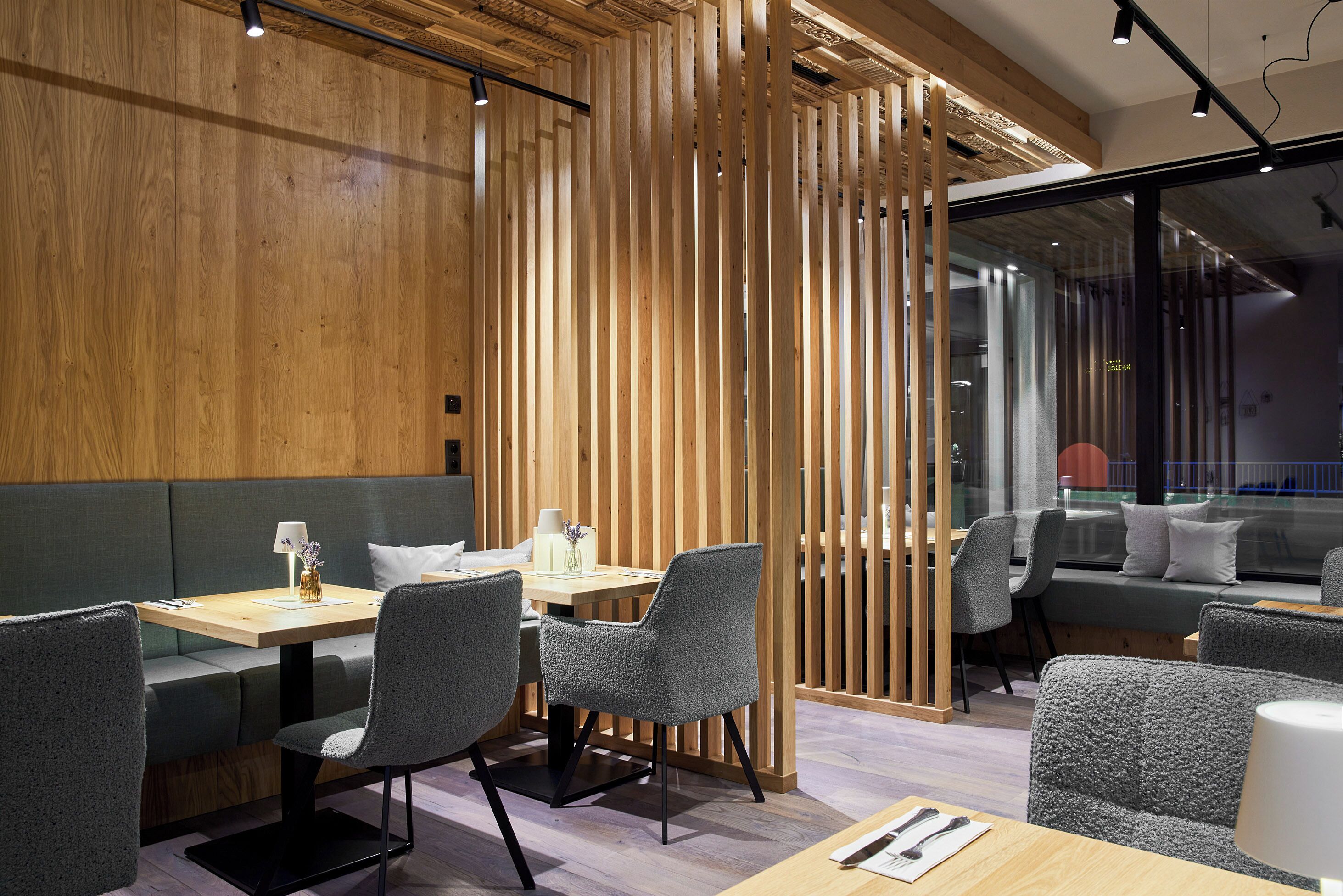 Un comedor moderno con paneles de madera, asientos tapizados en gris y una partición de vidrio.