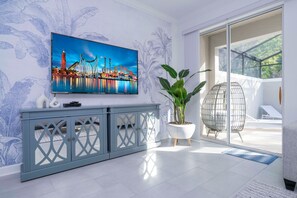 Un salon moderne avec un grand téléviseur à écran plat fixé au mur, une console grise, une plante en pot et une porte en verre donnant sur un espace extérieur.