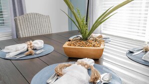 A dining table set with blue placemats, white napkins, and silverware. A wooden bowl with pebbles and a green plant is on the table.