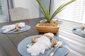 A dining table set with placemats, cutlery, and a centerpiece with a plant and pebbles.