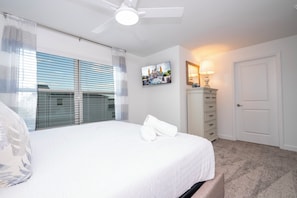 Ein Schlafzimmer mit einem Bett, einem Deckenventilator, einem Fernseher, einer Kommode und einer Tür.