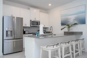 A modern kitchen with stainless steel appliances, a central island with bar stools, and a large window with a view.
