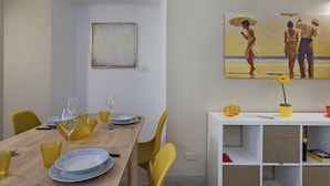A dining area with a wooden table set for four, yellow chairs, and a white cabinet with shelves. - Raibetta Apartments by Wonderful Italy (Genoa)