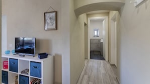 A hallway with a TV on a white shelf, a framed picture on the wall, and a small window in the background. - Raibetta Apartments by Wonderful Italy (Genoa)