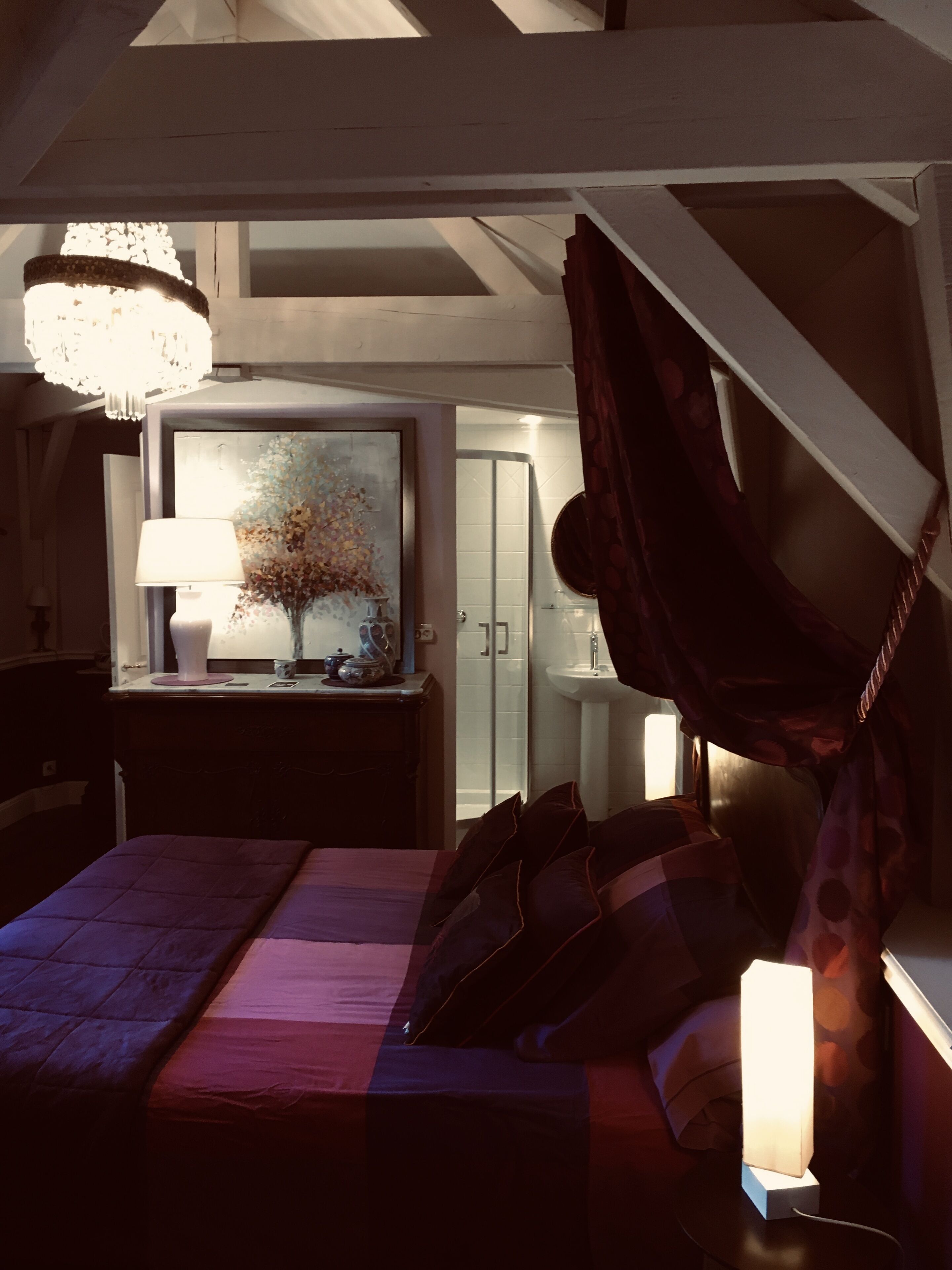 A bedroom with a bed, a bedside table with a lamp, a painting, and a nightstand with a lamp.