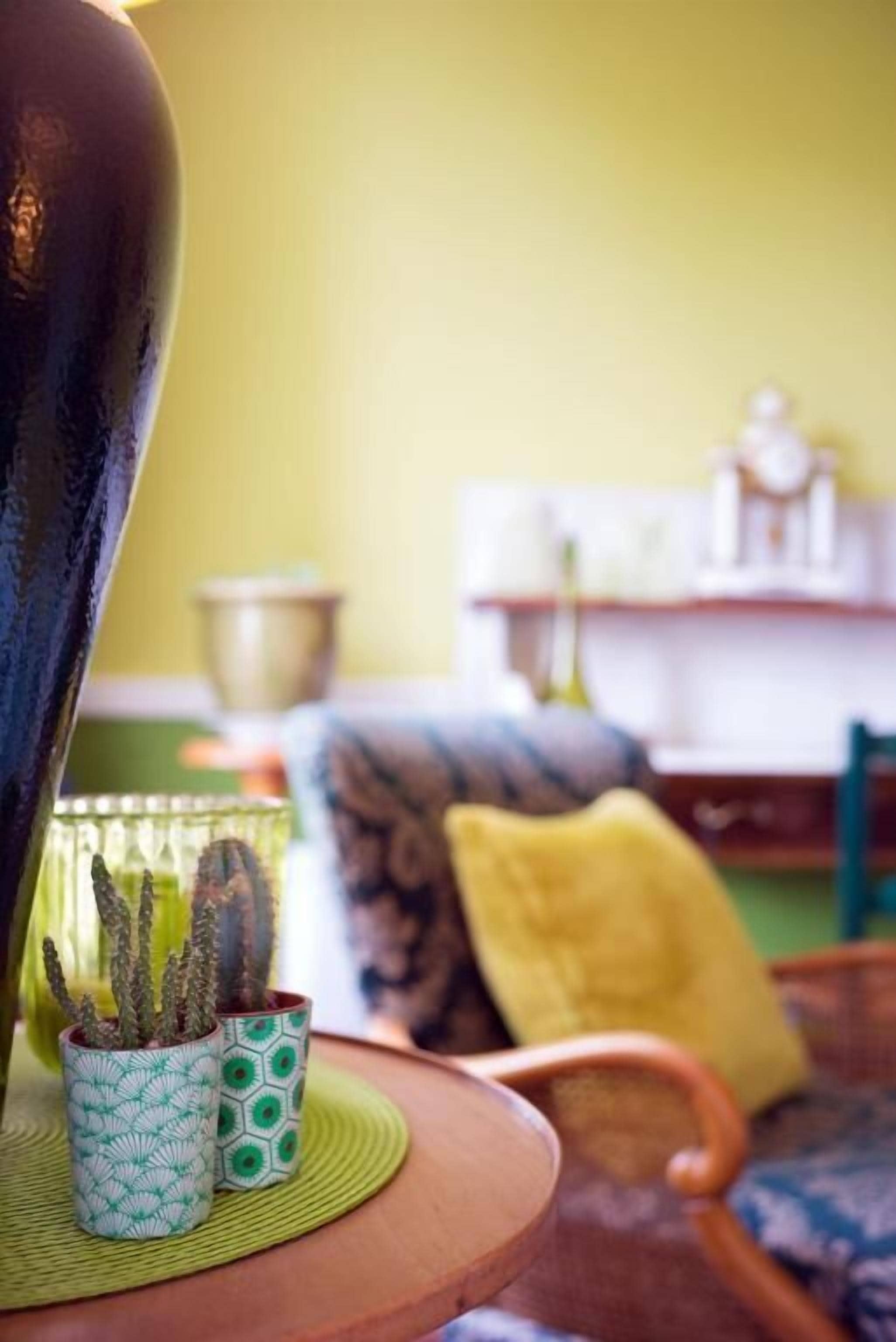Une pièce avec une table ronde en bois, deux tasses à motifs représentant des cactus, un coussin jaune et une chaise.