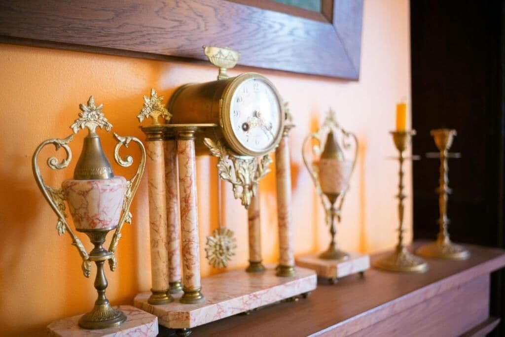 Een verzameling antieke klokken en decoratieve objecten op een plank tegen een muur.