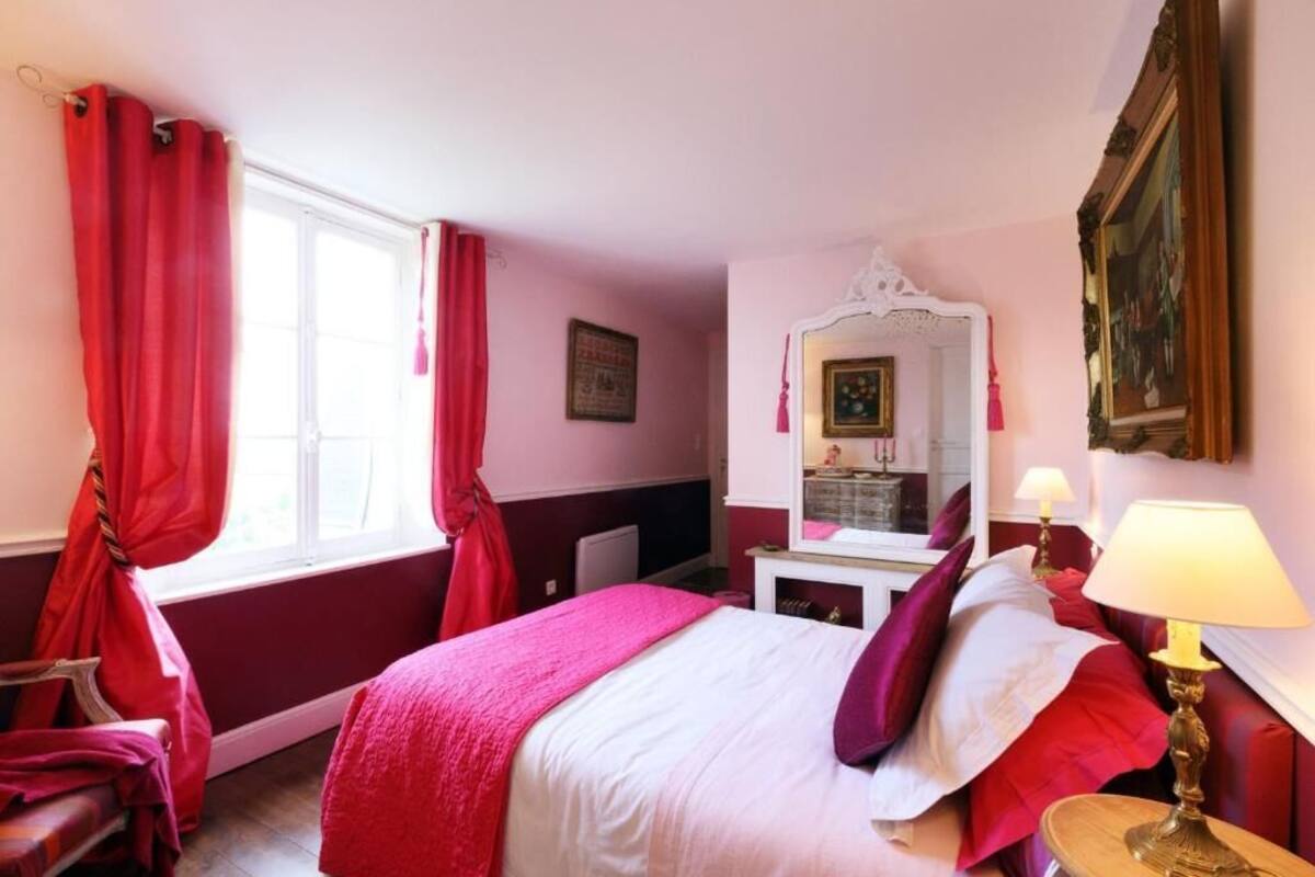 Ein Hotelzimmer mit einem Bett, einem Fenster mit roten Vorhängen, einem Spiegel und einer Lampe.