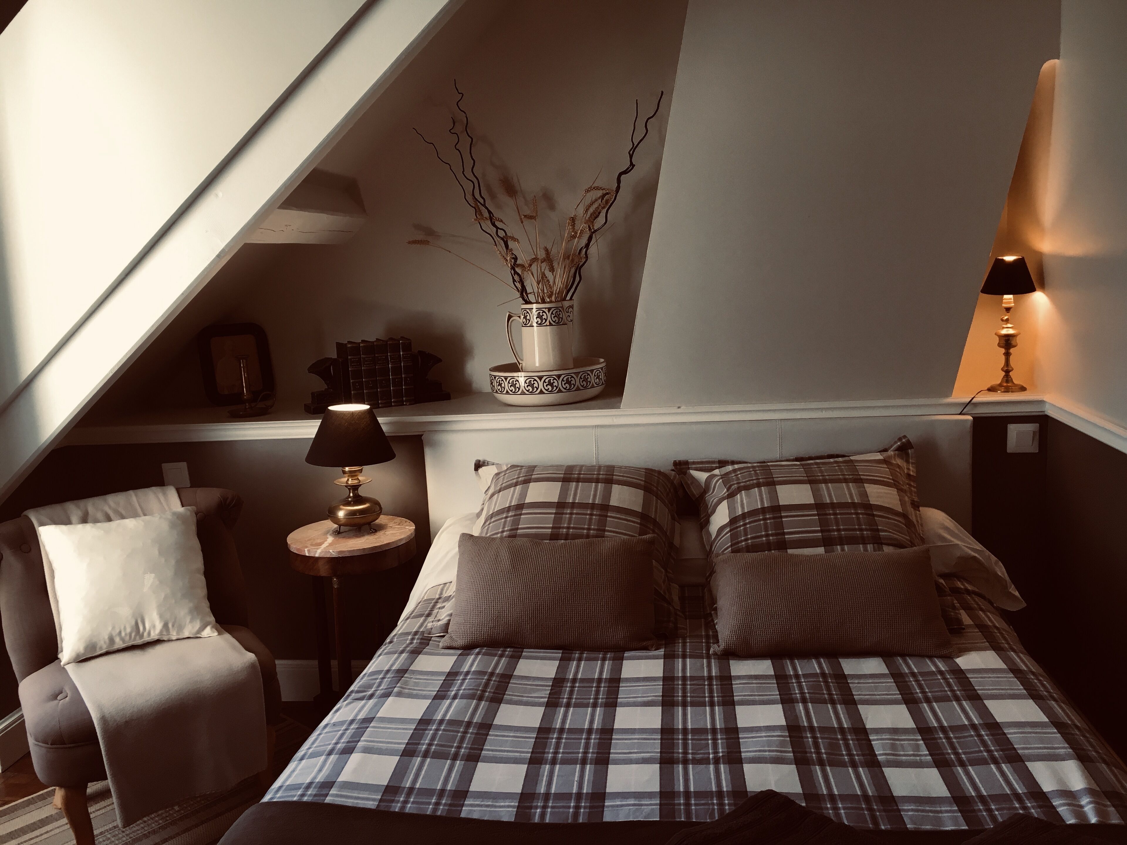 A bedroom with a bed, a chair, a lamp, and a decorative vase on a shelf.