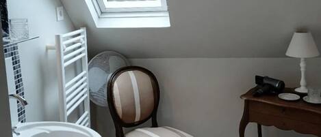 Une petite salle de bain avec un puits de lumière, un lavabo blanc, une chaise et une table en bois sur laquelle se trouve une lampe.