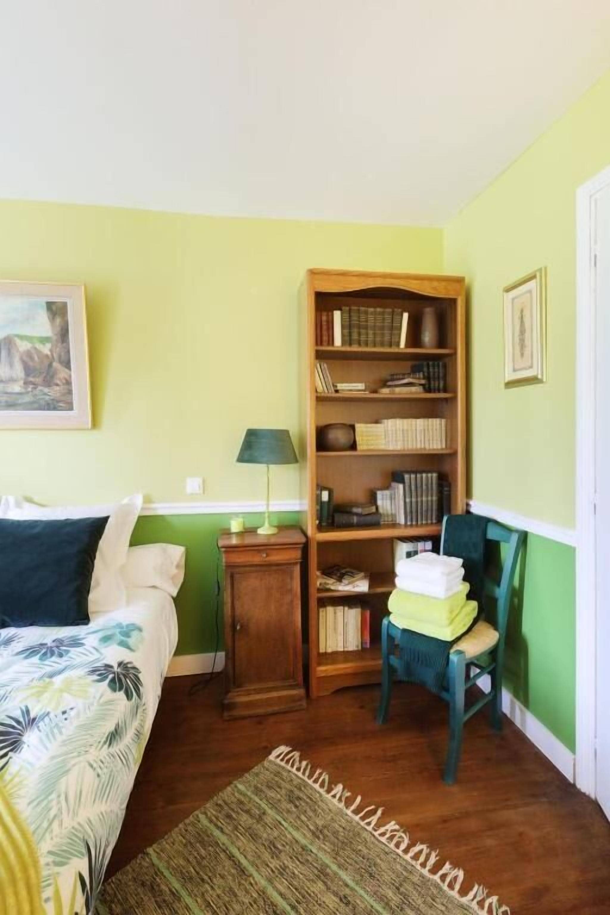 A room with a bed, a bookshelf, a chair, and a lamp.