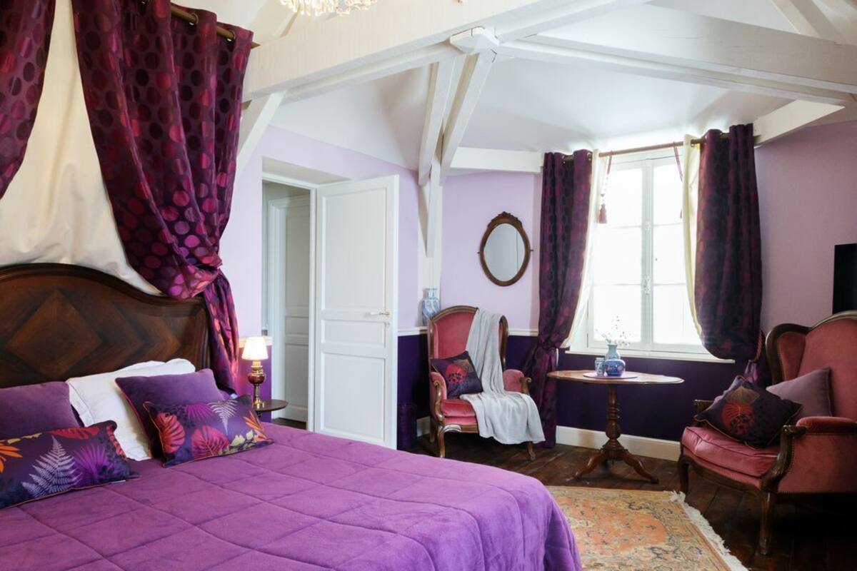 Ein Schlafzimmer mit einem großen Bett, einer Kristallleuchtre, Holzboden und einem Vorhangfenster.