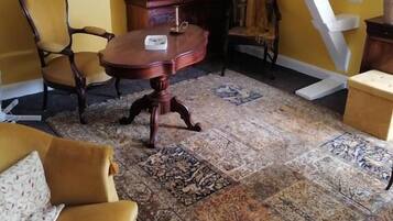 A room with a wooden desk, two chairs, a patterned rug, and a yellow wall.