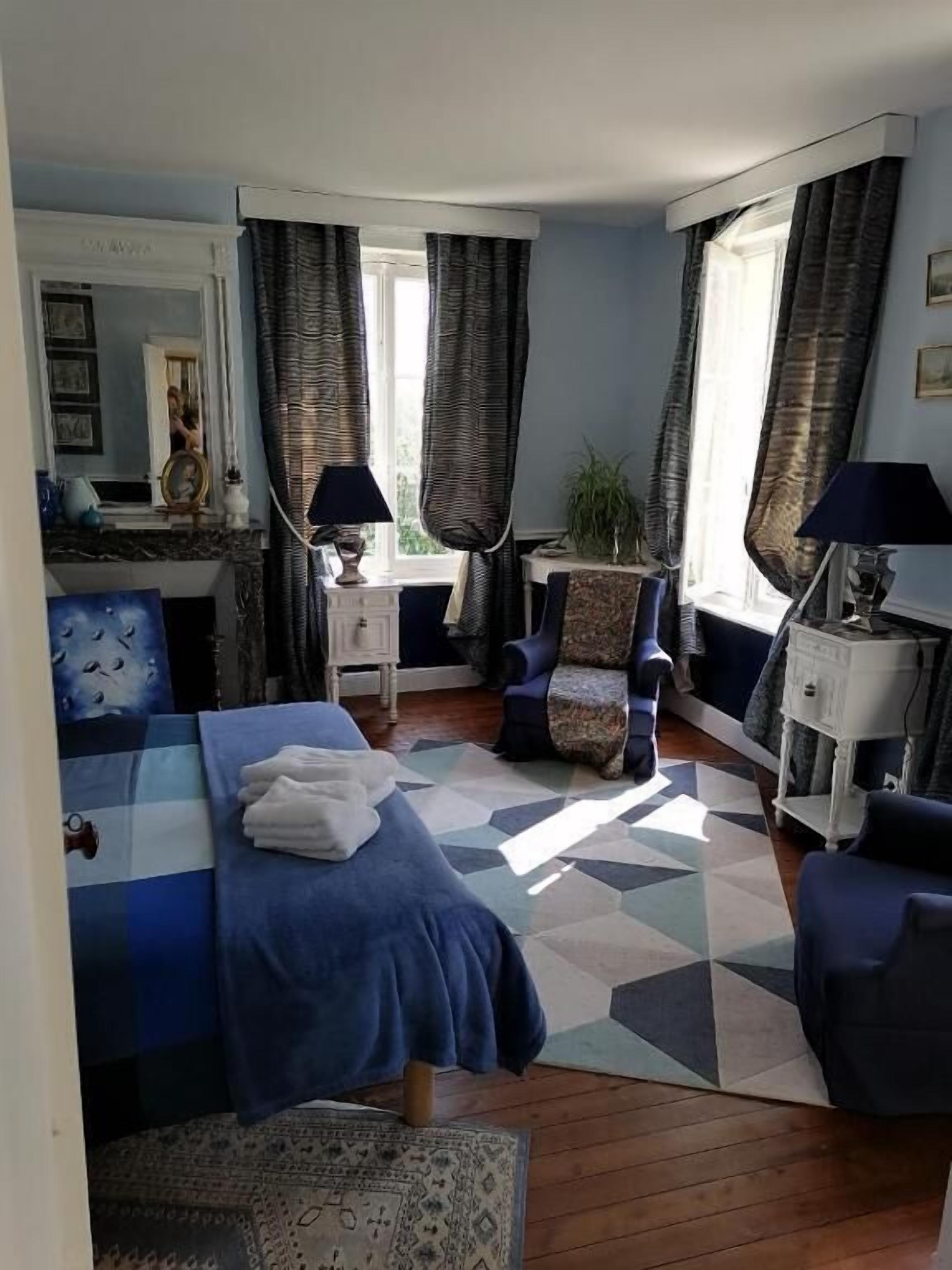 Een slaapkamer met een bed, een stoel, een nachtkastje en een raam met gordijnen.