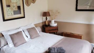 A neatly made bed with a white and beige duvet, a small bedside table with a lamp, and a framed picture on the wall.