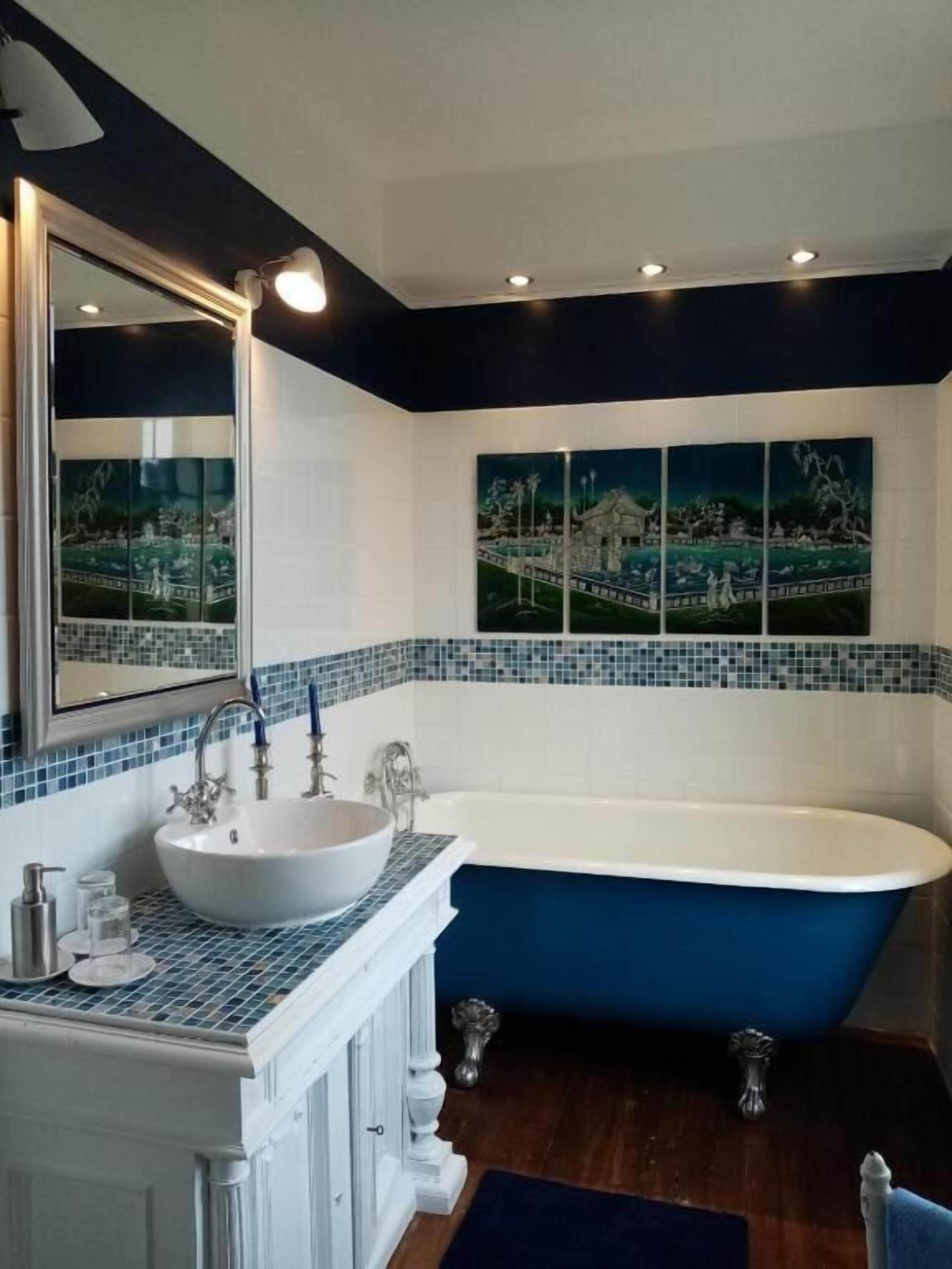 A bathroom with a freestanding bathtub, a large mirror, and a mosaic tile border.