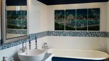 A bathroom with a freestanding bathtub, a large mirror, and a mosaic tile border.