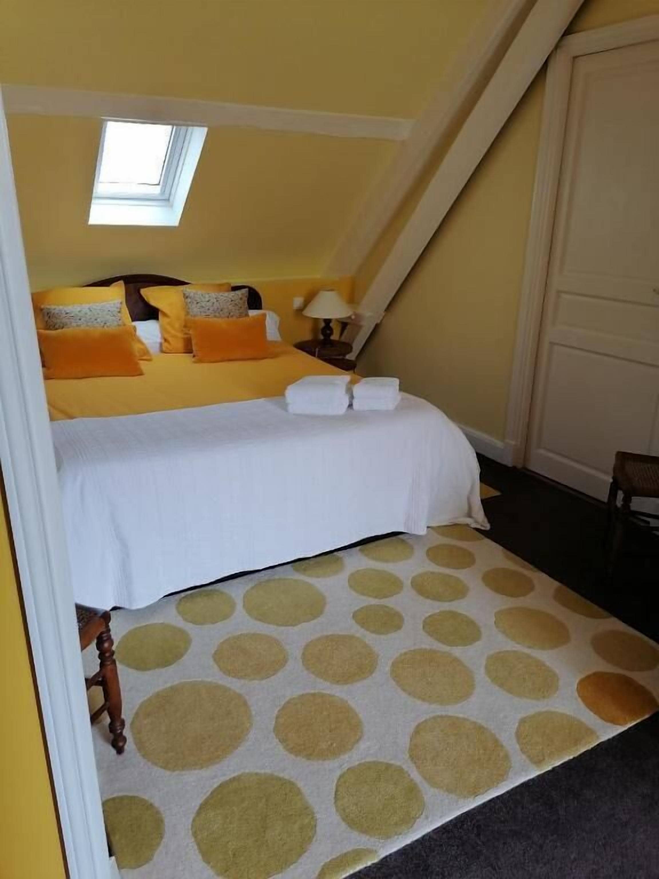 Un dormitorio con cama, almohadas, una mesita de noche, una lámpara y una ventana.