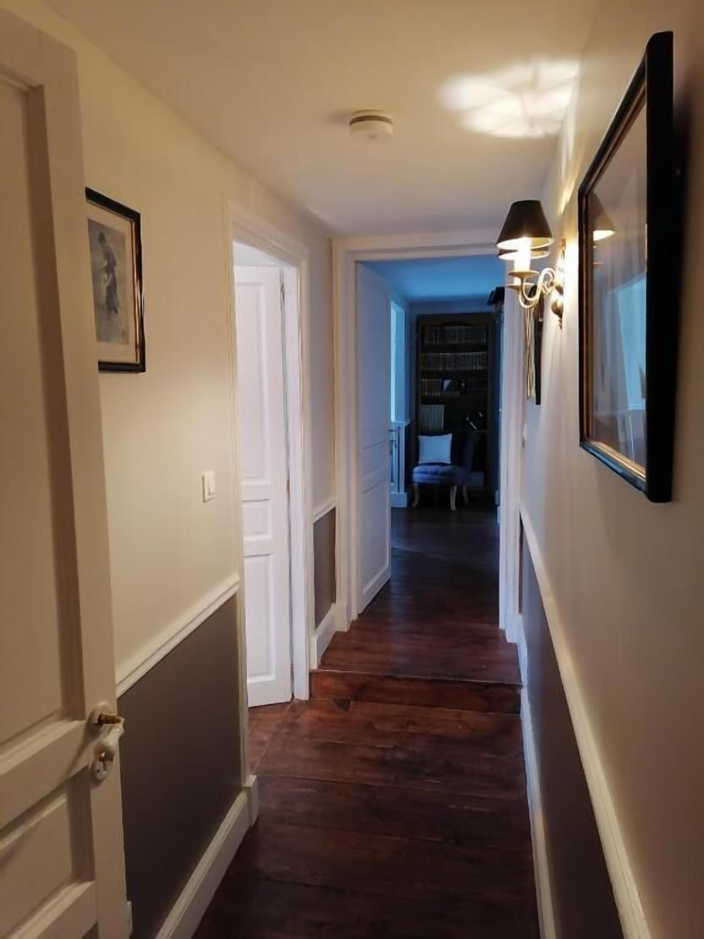 A hallway with wooden flooring, white walls, and a door on the left.