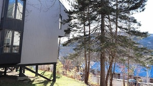 Une maison moderne à deux étages, dotée d’un toit en pente, de grandes fenêtres et offrant une vue sur une zone boisée.