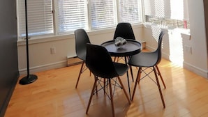 Un espace repas comprenant une table et des chaises, de grandes fenêtres équipées de stores et un lampadaire.