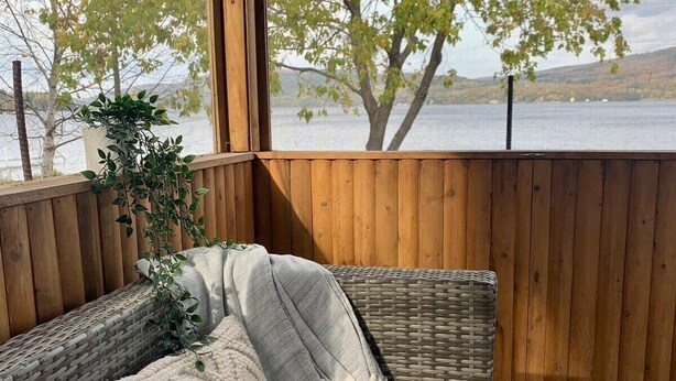 A covered outdoor seating area with wicker furniture and a view of a lake.